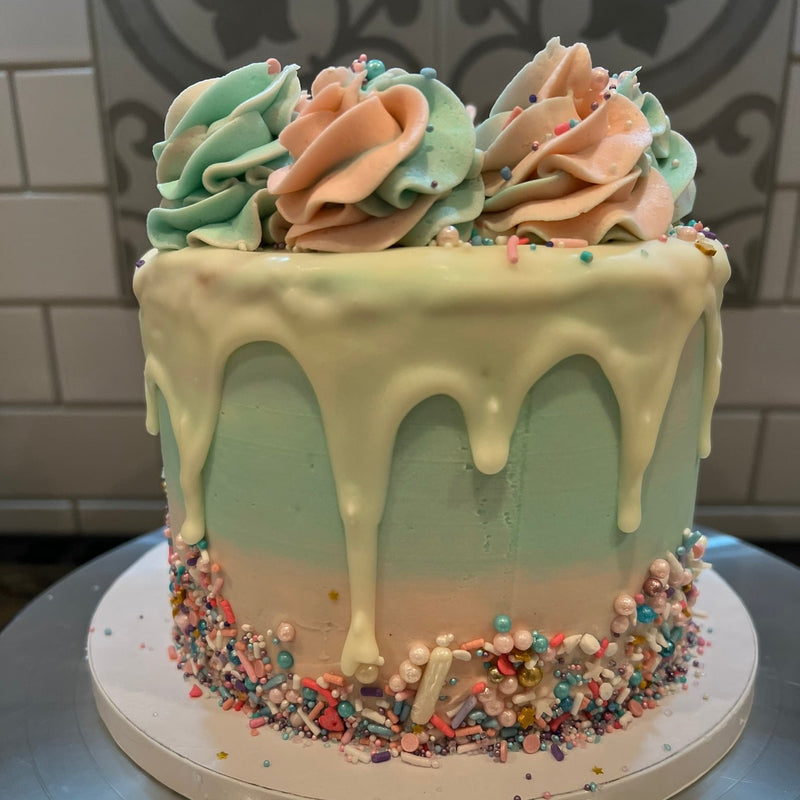Decorative cake with pastel colors and sprinkles on a metallic surface.