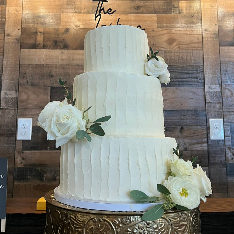 White wedding cake with floral decorations against a wooden wall.