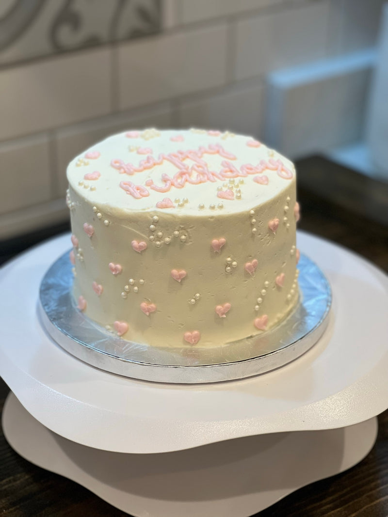 White cake with pink decorations on a white stand against a tiled wall background